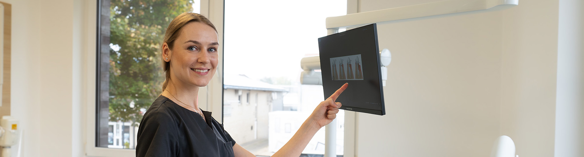 Zahnmedizinische Assistentin zeigt einer Patientin Zahnaufnahmen auf dem Monitor mithilfe einer intraoralen Kamera.
